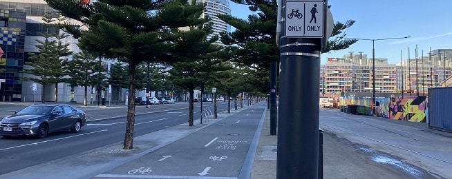 A cycle path on the left of the image separated from a footpath by a large pole with black and white sign directing people riding and walking to either side.