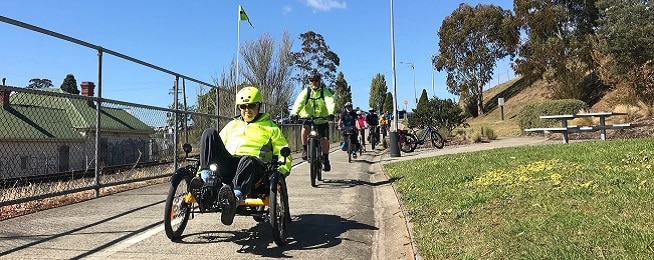 A line of bicycles riding down the Intercity Cycleway with a man in a recumbent wearing a yellow jacket and helmet leading the way.