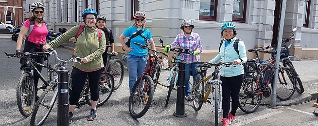 A group of women stand in a line with bicycle out the front of an old sandstone building on Hobart's waterfront.